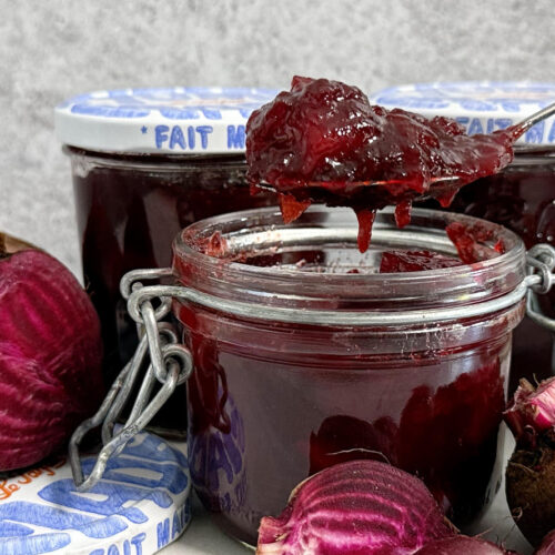 Easy Sweet and Spicy Beetroot chutney being spooned out of a jar with more jars in the background and freshly cut beetroot.
