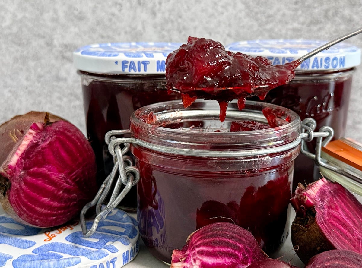 Easy Sweet and Spicy Beetroot chutney being spooned out of a jar with more jars in the background and freshly cut beetroot.